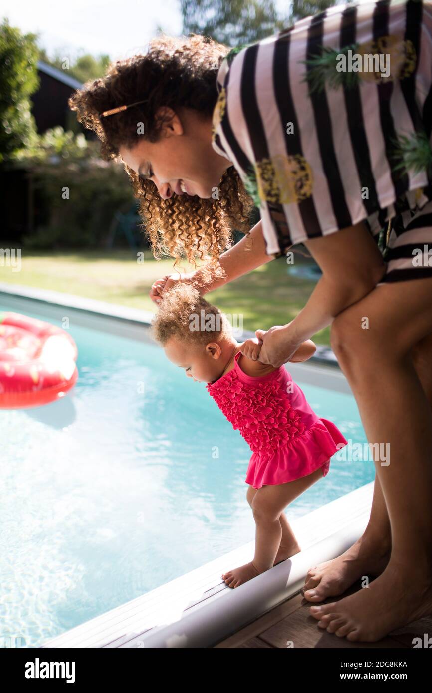 Mother helping curious toddler daughter at edge of swimming pool Stock Photo