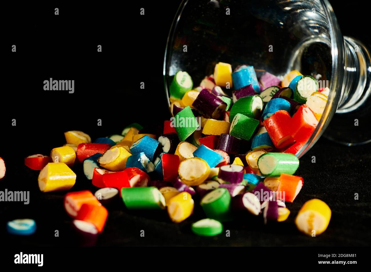 sugar candies falling from glass container on black table background. Empty space for text Stock Photo