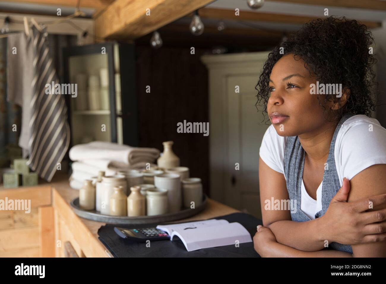 Thoughtful female shop owner at counter looking away in anticipation Stock Photo