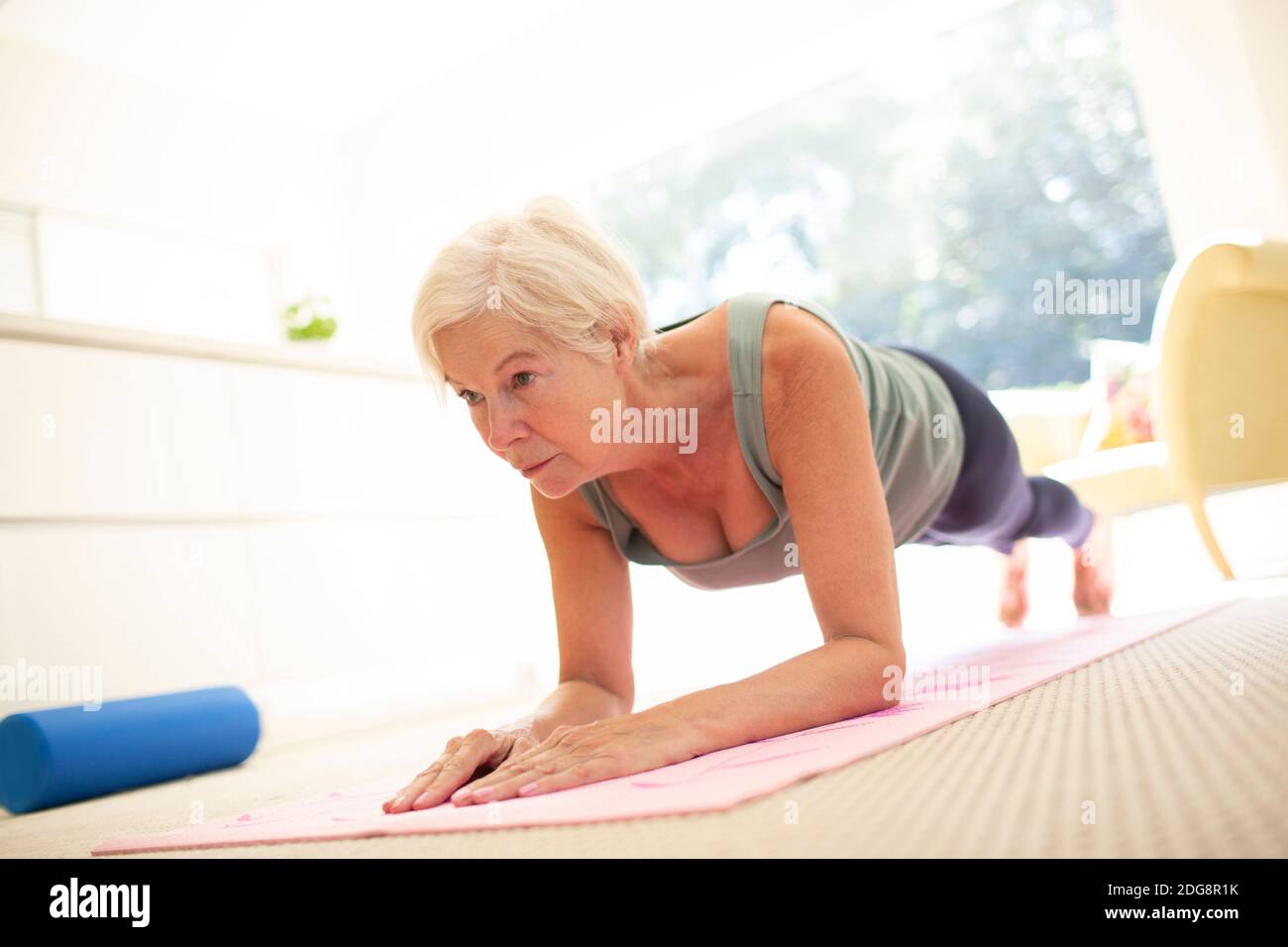 Focused senior woman practicing plank exercise on yoga mat at home Stock Photo