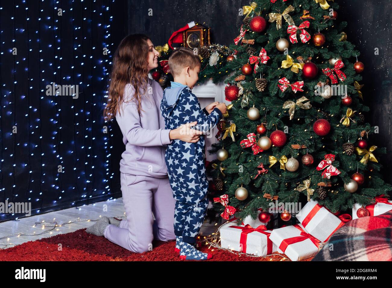 Mom and son decorate Christmas tree with gifts lights garland Stock