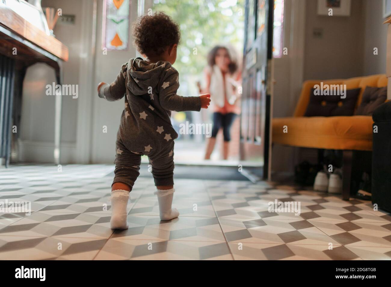 Cute baby girl in star pajamas walking to mother at open doorway Stock Photo