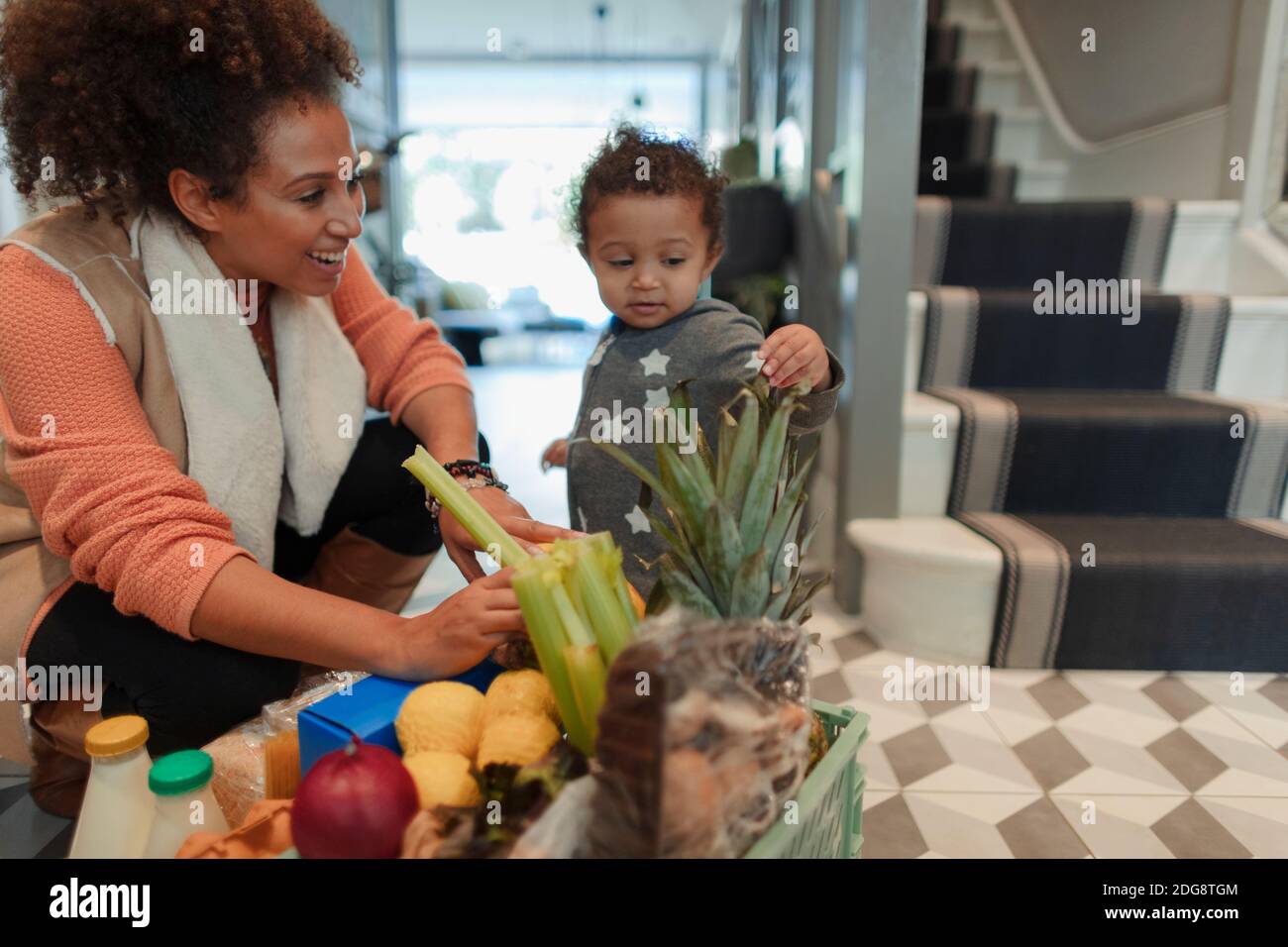 Cute baby daughter helping mother unpack grocery delivery Stock Photo