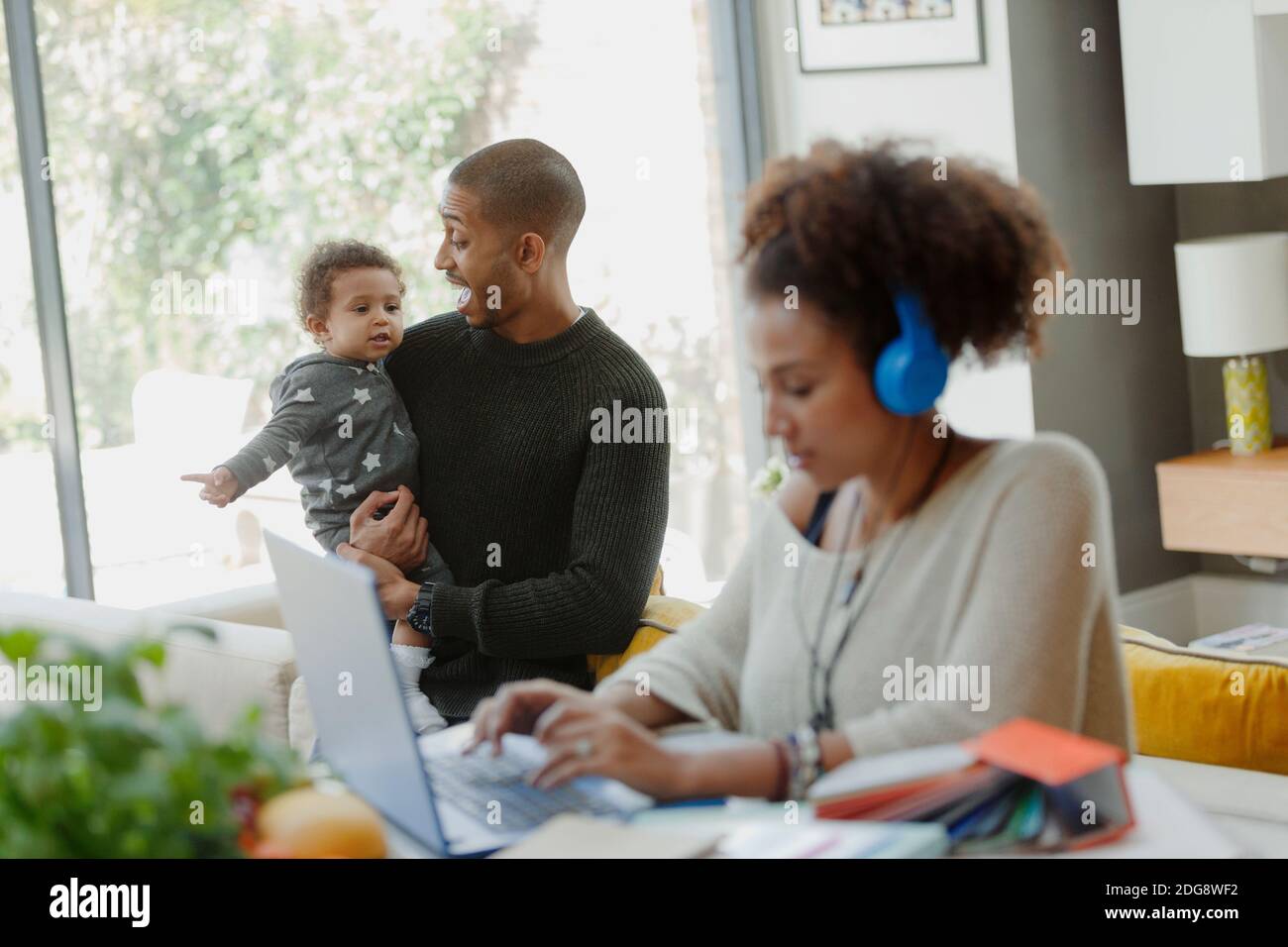 Father holding baby daughter behind working mother at laptop Stock Photo