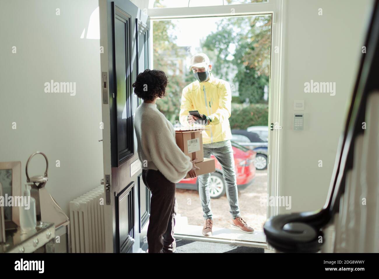 Woman receiving package from delivery man in face mask at front door Stock Photo
