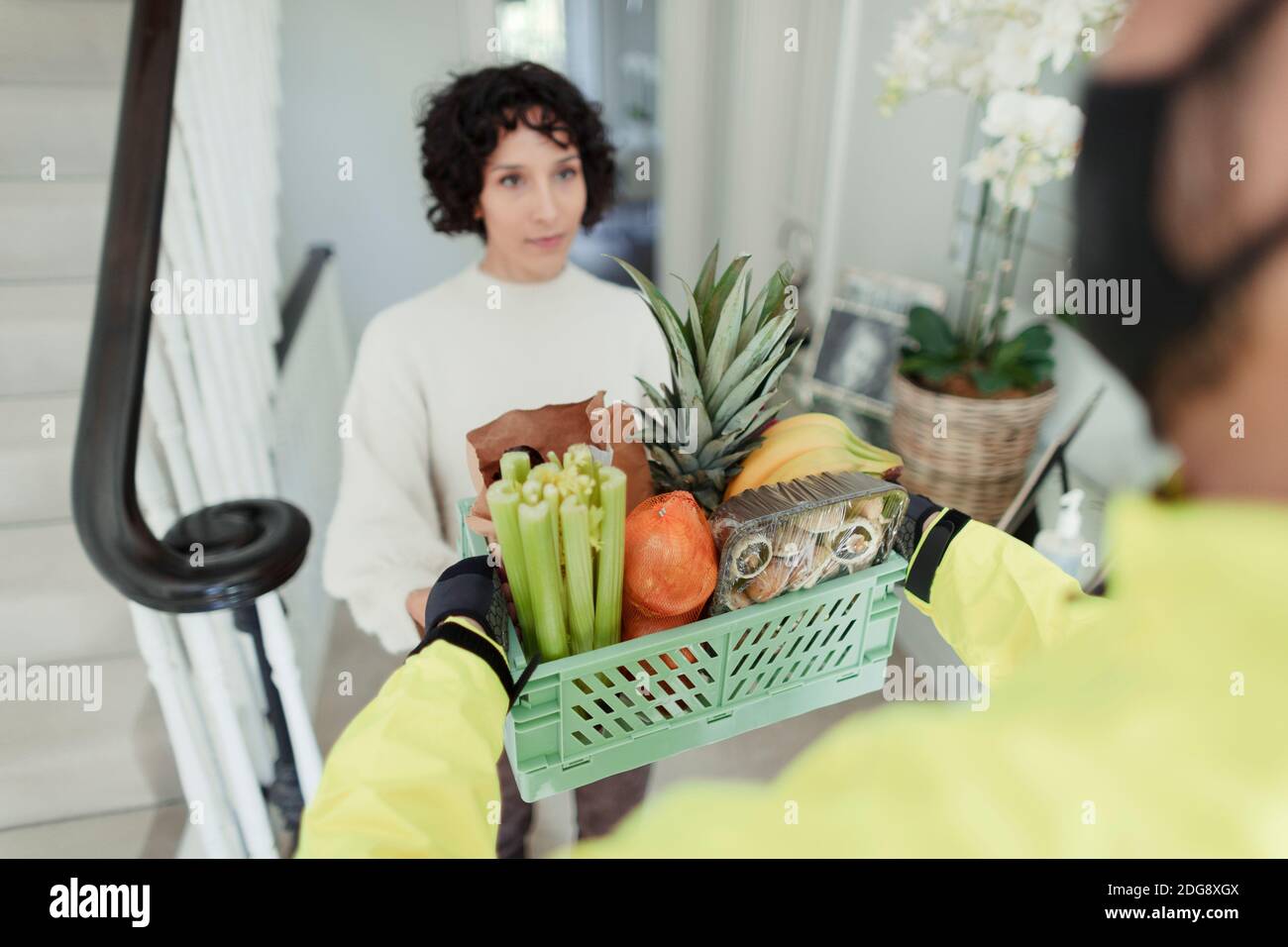 Woman receiving grocery delivery from courier in face mask Stock Photo