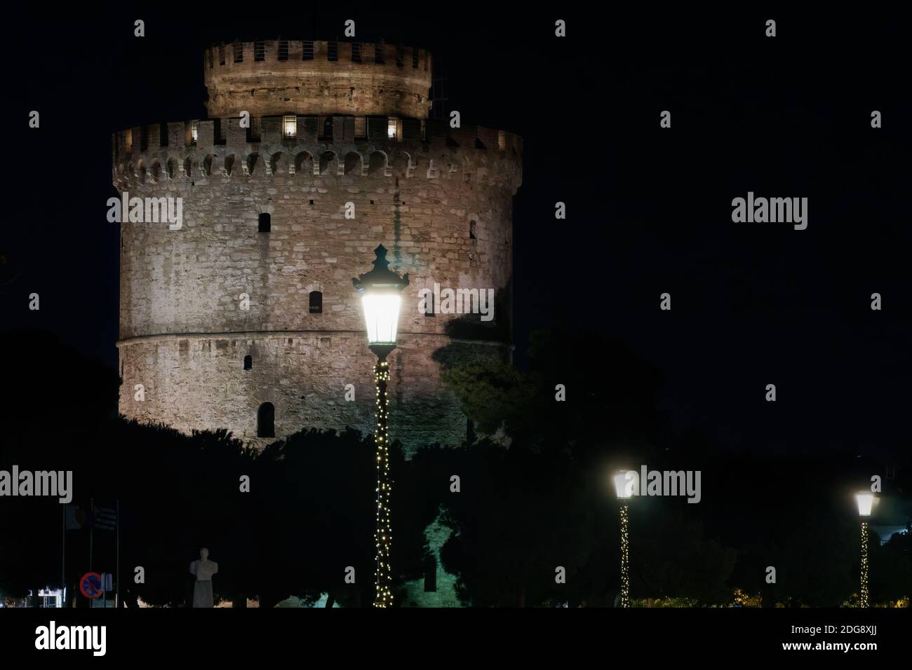 Thessaloniki Greece night view of The White Tower with Christmas lights decoration around. The city's landmark with illuminated seasonal instalments under dark sky. Stock Photo