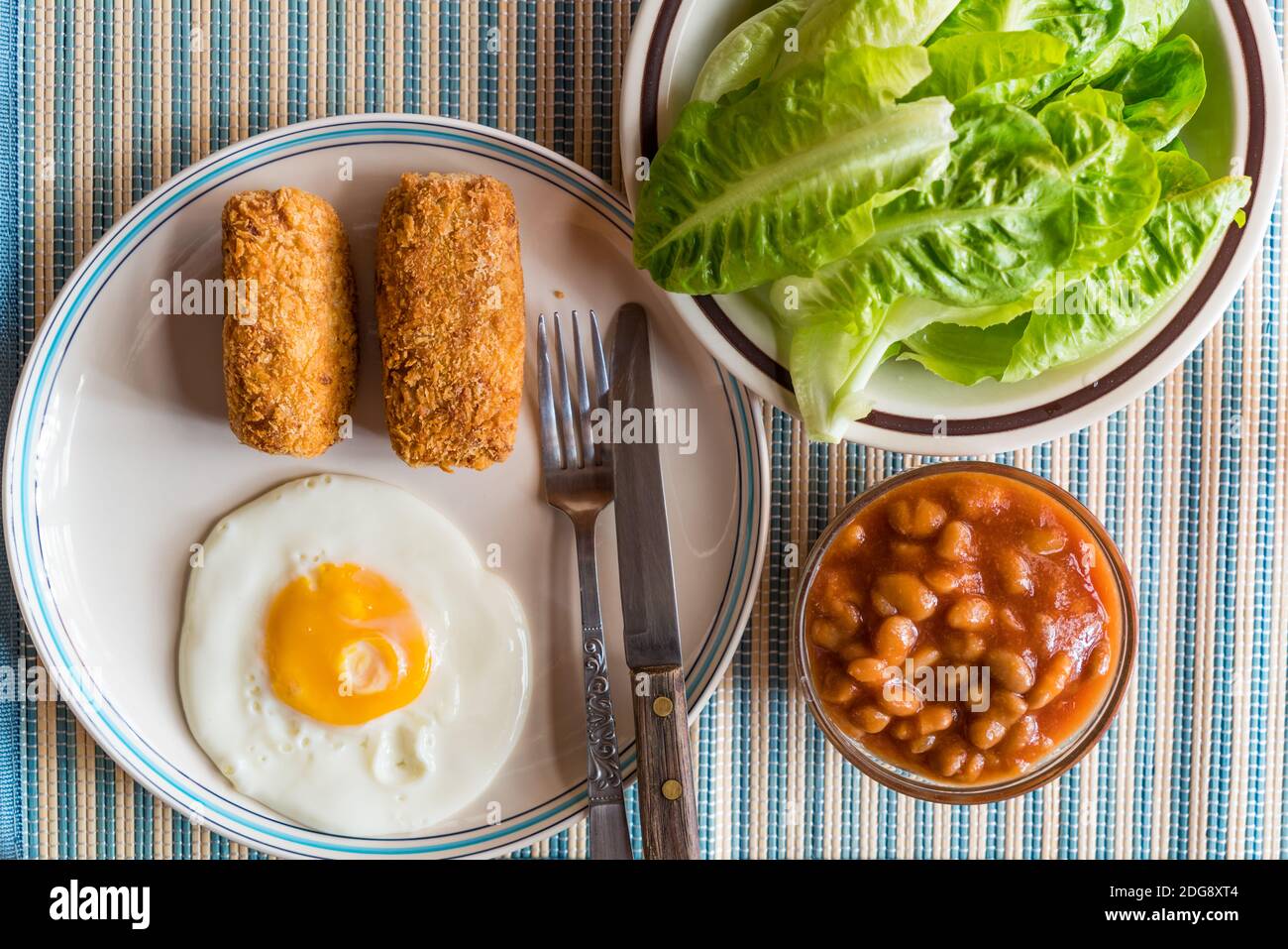 Croquettes, fried egg, fresh vegetables, white kidney beans in tomato