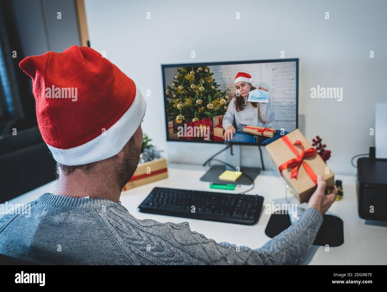 Sad man with mask on video call with girlfriend in self isolation missing celebrating christmas and new year face to face. Virtual celebrations and CO Stock Photo