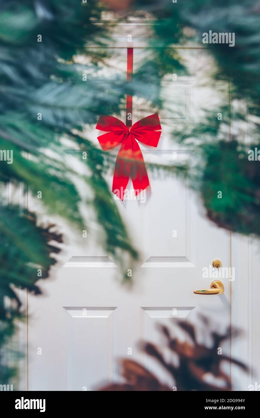White appartment door with seasonal greens out of focus and red bow. Holiday decorations concept Stock Photo