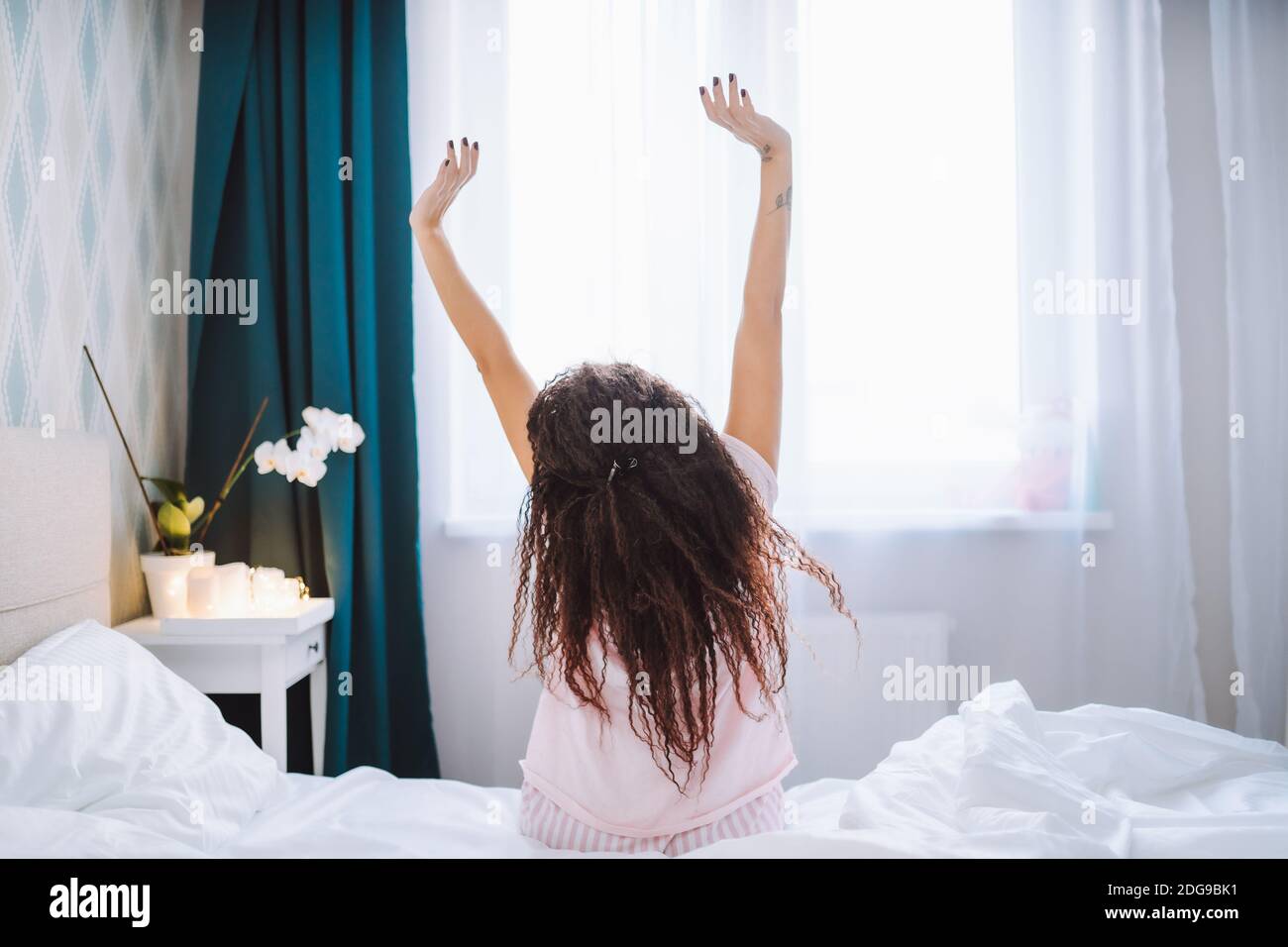 Young long-haired woman outstretching her arms sitting on the bed after ...