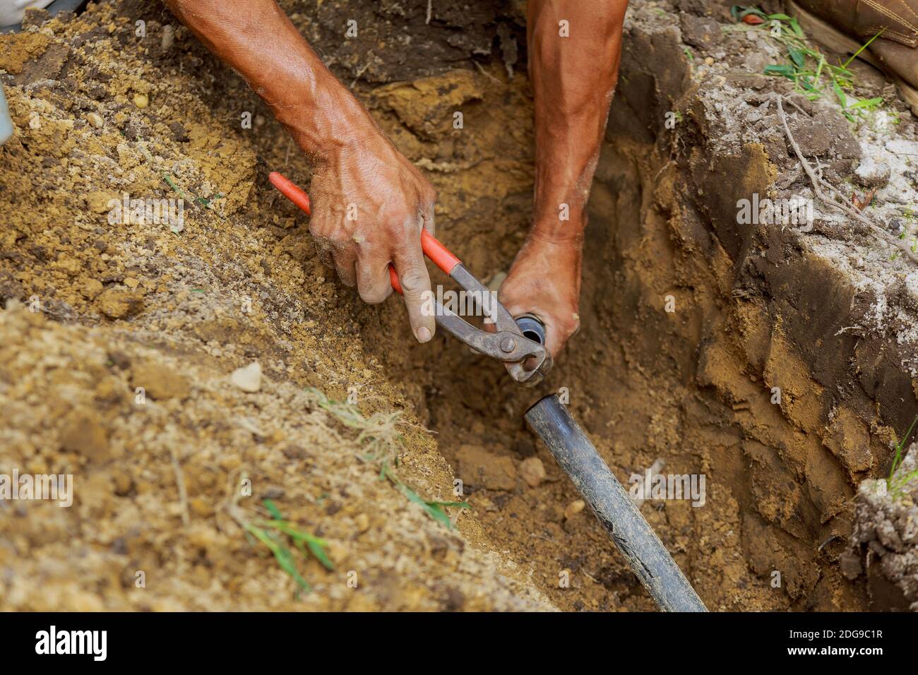 Man Applying Solvent Primer and Cement to PVC Pipes as Part of Installation of Underground automatic Sprinkler System Stock Photo