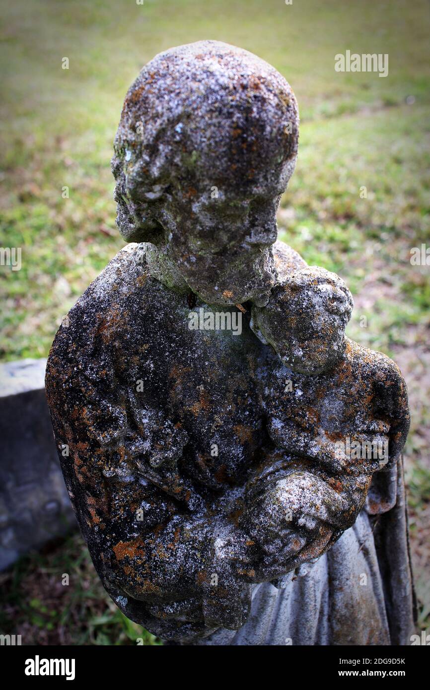 vignette of a small antique deeply weathered and darkly stained cement figurine of Christ tenderly holding a child Stock Photo