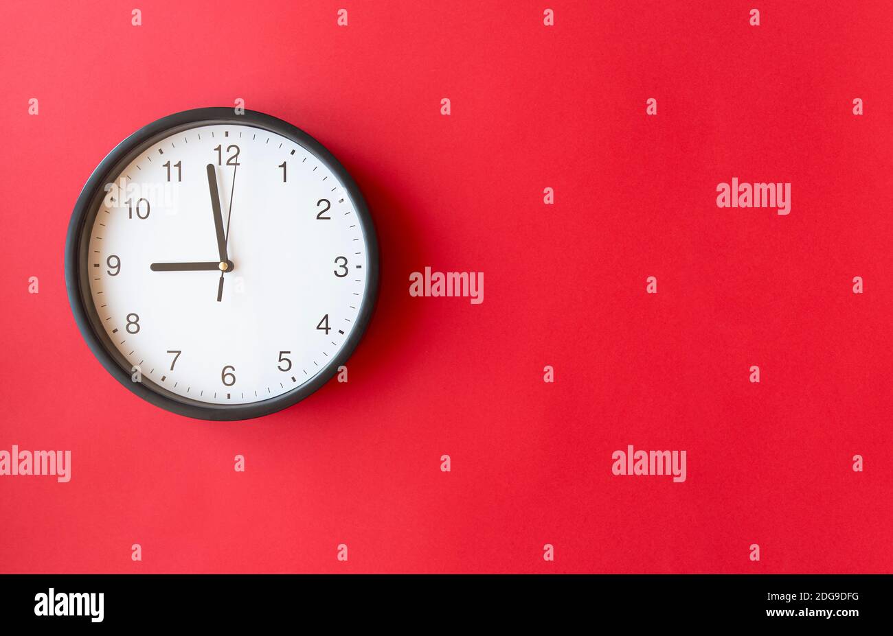 Round wall clock on red surface showing 9 o’clock, layout, top view, place for text Stock Photo