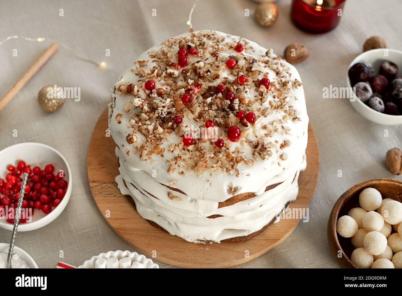 Preparing food for Christmas dinner. Homemade Christmas cake with white icing sugar, nuts and red cranberries Stock Photo