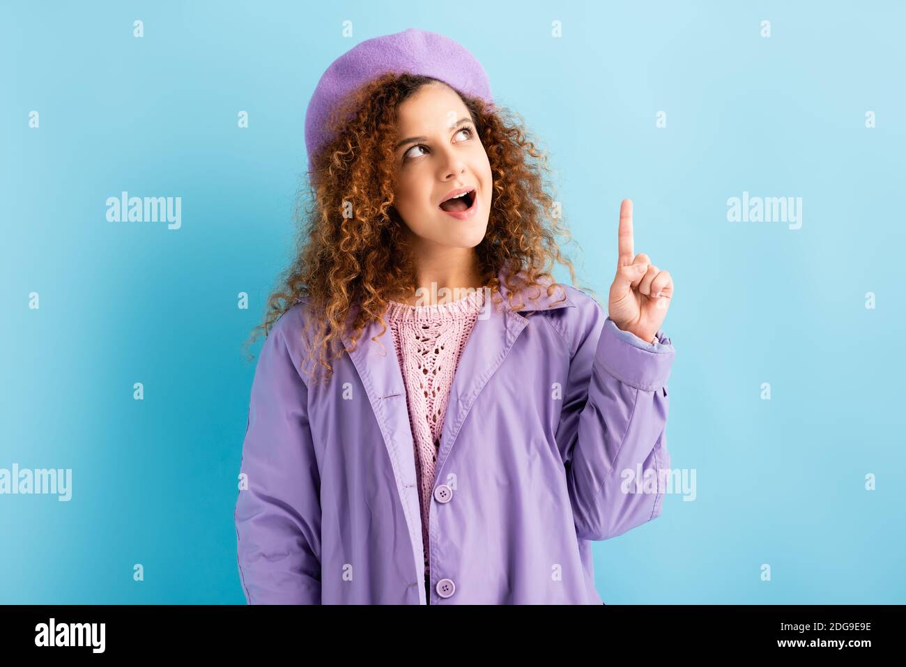 curly woman in beret and coat having idea on blue Stock Photo - Alamy