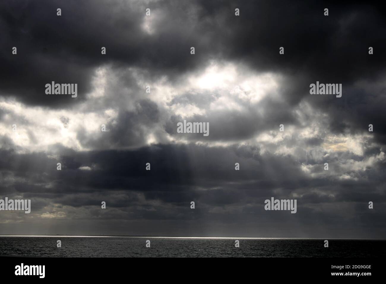 soft subtle rays of sunlight filter through the thick dark clouds down onto the surface of the large lake Stock Photo