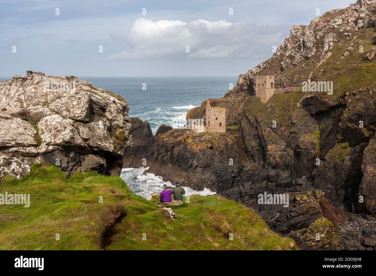A hiking couple sit to admire the view of the famous Crowns Engine Houses, Botallack Mine, West Penwith, Cornwall, UK Stock Photo