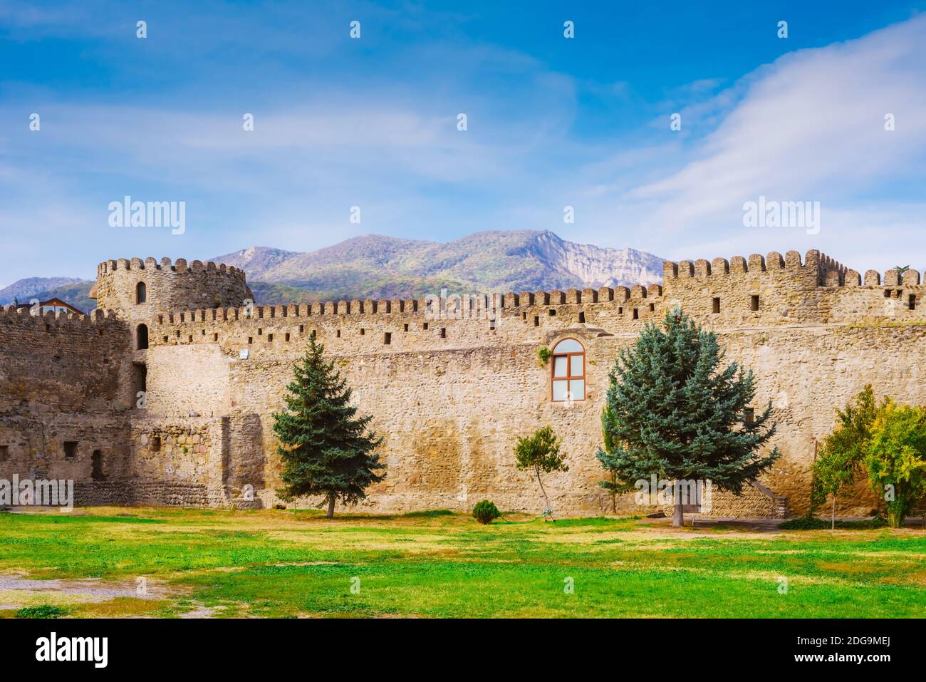 The yard of the ancient monastery with trees, stone wall and mountains ...