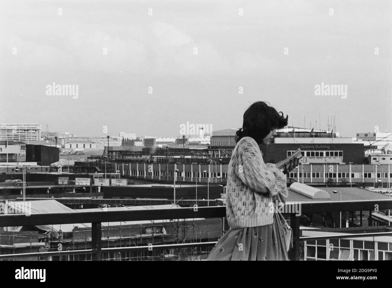 Archival monochrome image of a young woman reading a book on the observation deck of Heathrow Airport, London, 1979, showing the Queen's Building by Frederick Gibberd, built 1955, demolished 2009 Stock Photo