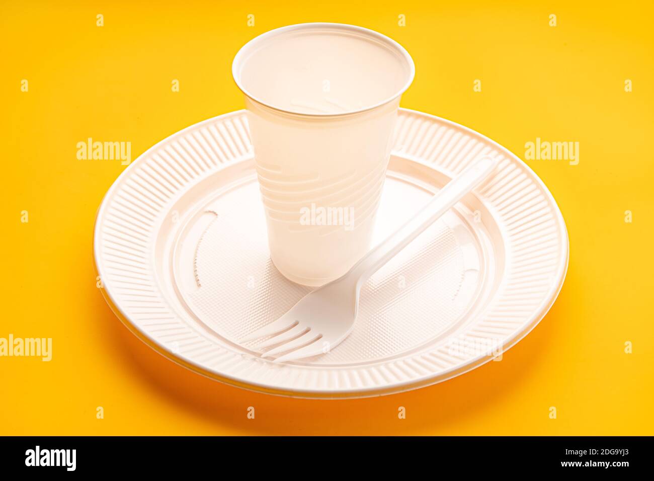 Plastic dishware. White vase, plate and fork on yellow background. Disposable plastic waste Stock Photo
