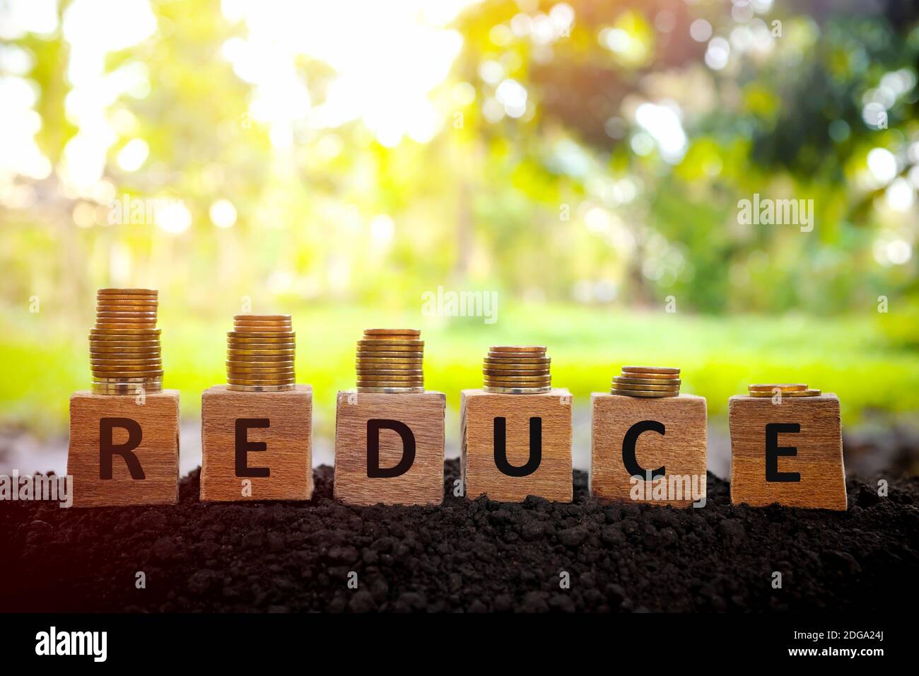 Price reduction, depreciation and devaluation concept. Decreasing stack of coins on wooden blocks at sunset on natural background. Stock Photo