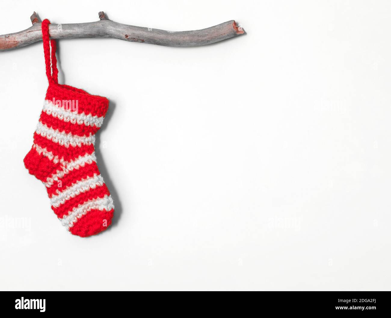 Christmas sock in a white-red strip hanging on a wooden branch on a white background Stock Photo