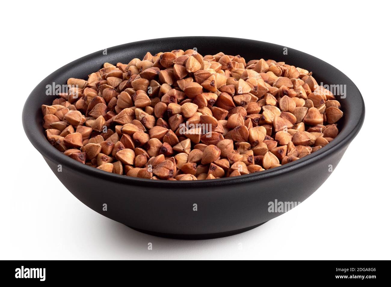 Raw toasted buckwheat in a black ceramic bowl isolated on white. High angle. Stock Photo