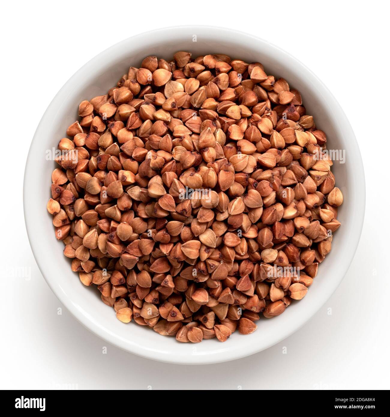 Raw toasted buckwheat in a white ceramic bowl isolated on white. Top view. Stock Photo