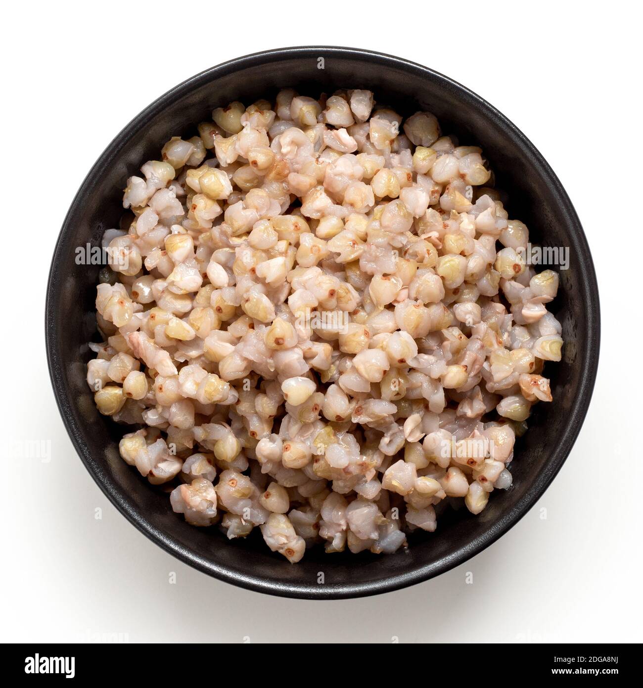 Cooked green buckwheat in a black ceramic bowl isolated on white.Top view. Stock Photo