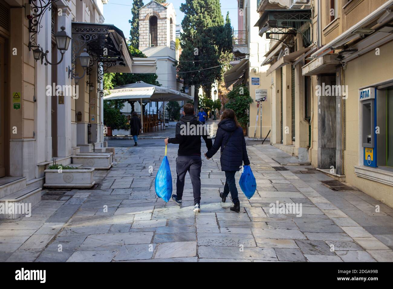 Athens city center, Greece. December 5 2020. Young couple holding garbage bags rear view, city center, Kydathinaion street, Plaka. Coronavirus pandemi Stock Photo