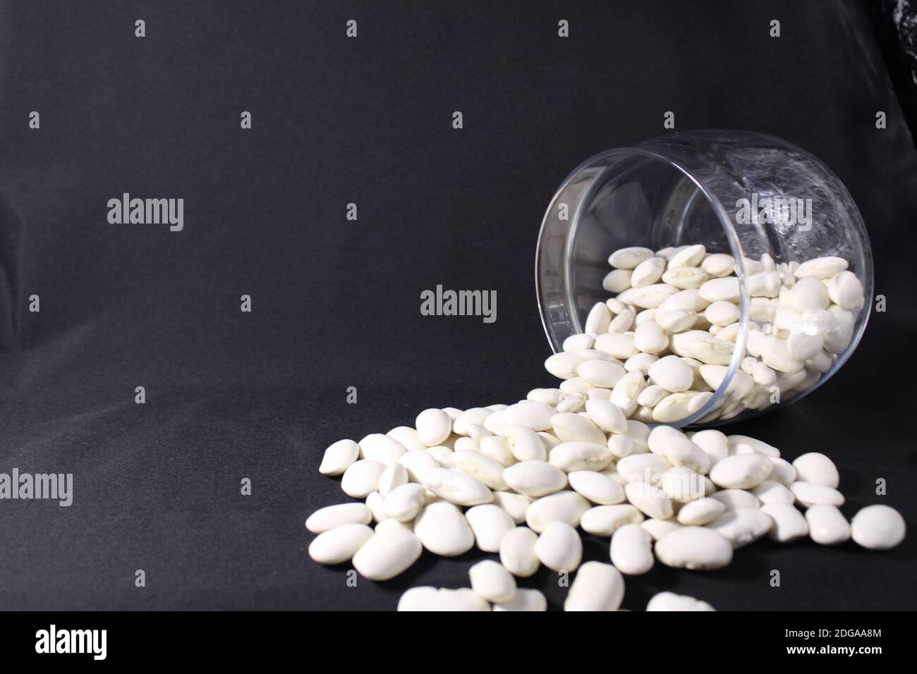 beans poured out of a glass jar on the black background of a copy of