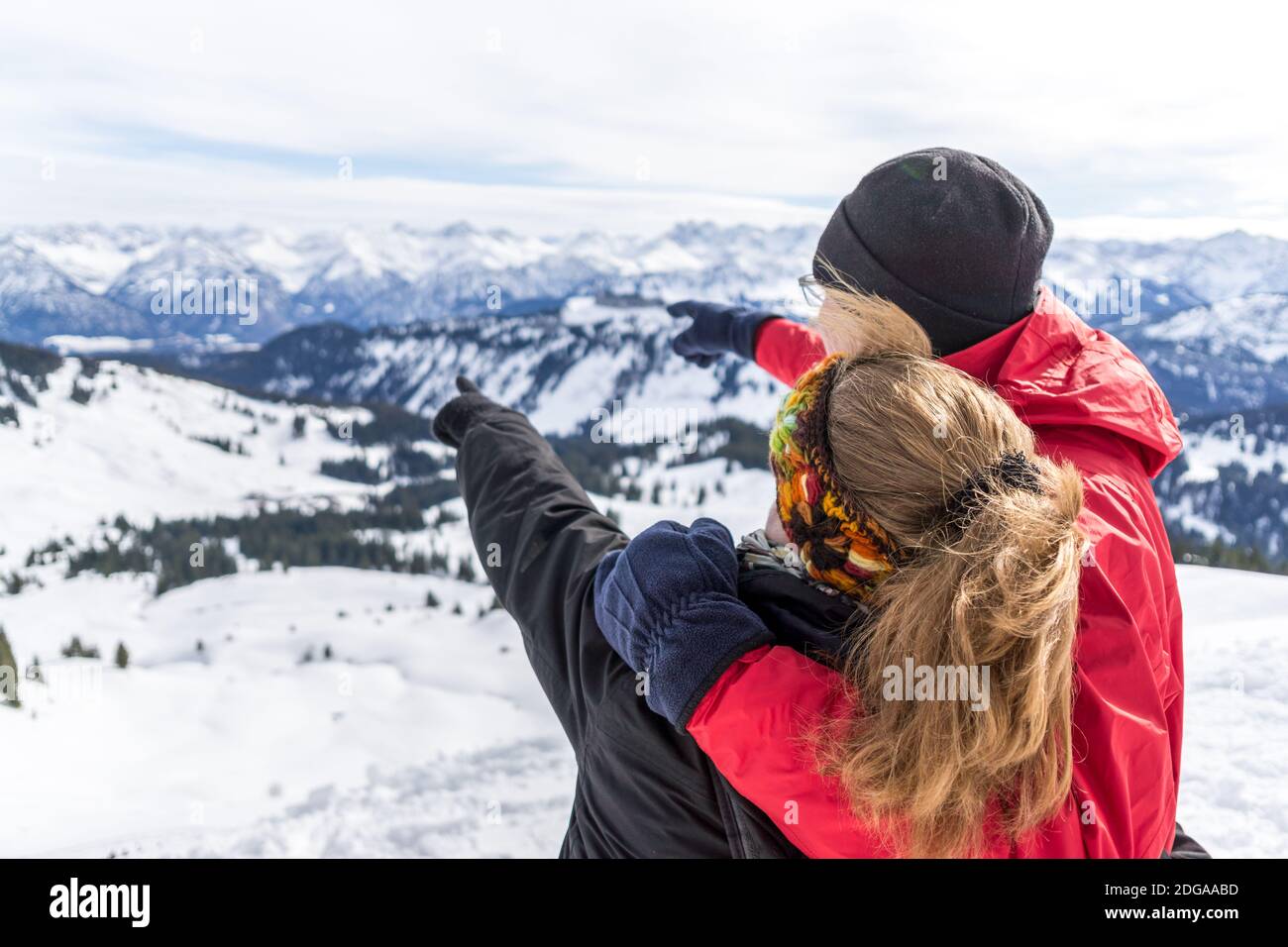 Senior couple is hiking in alpine snow winter mountains enjoying panorama view and pointing with finger to mountain peaks. Allgau, Bavaria, Germany. Stock Photo