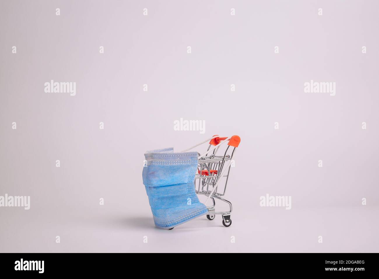 Safe and online shopping on quarantine concept. Shopping cart with protective medical mask against coronavirus. White background, copy space. Stock Photo