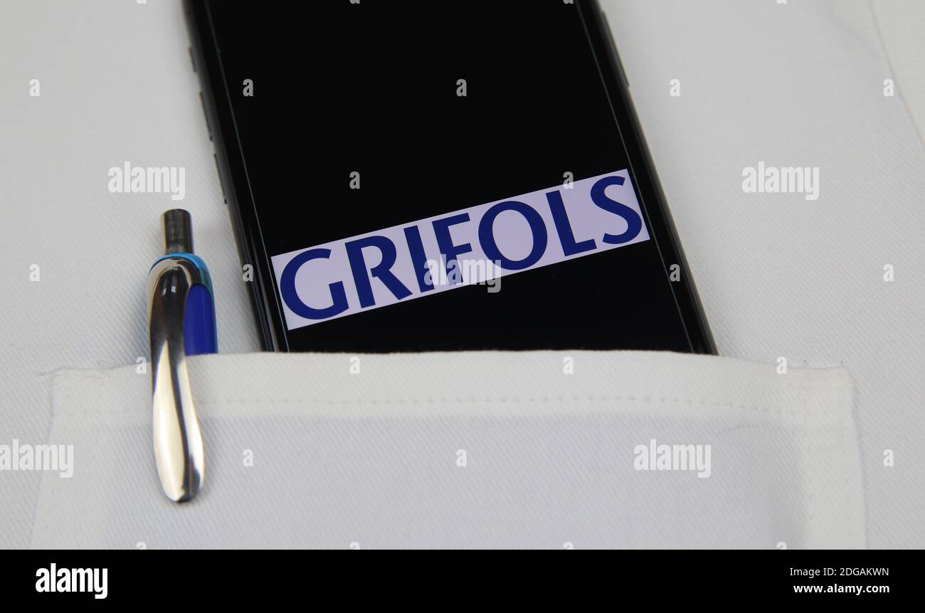 Viersen, Germany - April 9. 2020: Close up of mobile phone screen with logo lettering of Grifols pharmaceutical company in pocket of white doctors coa Stock Photo