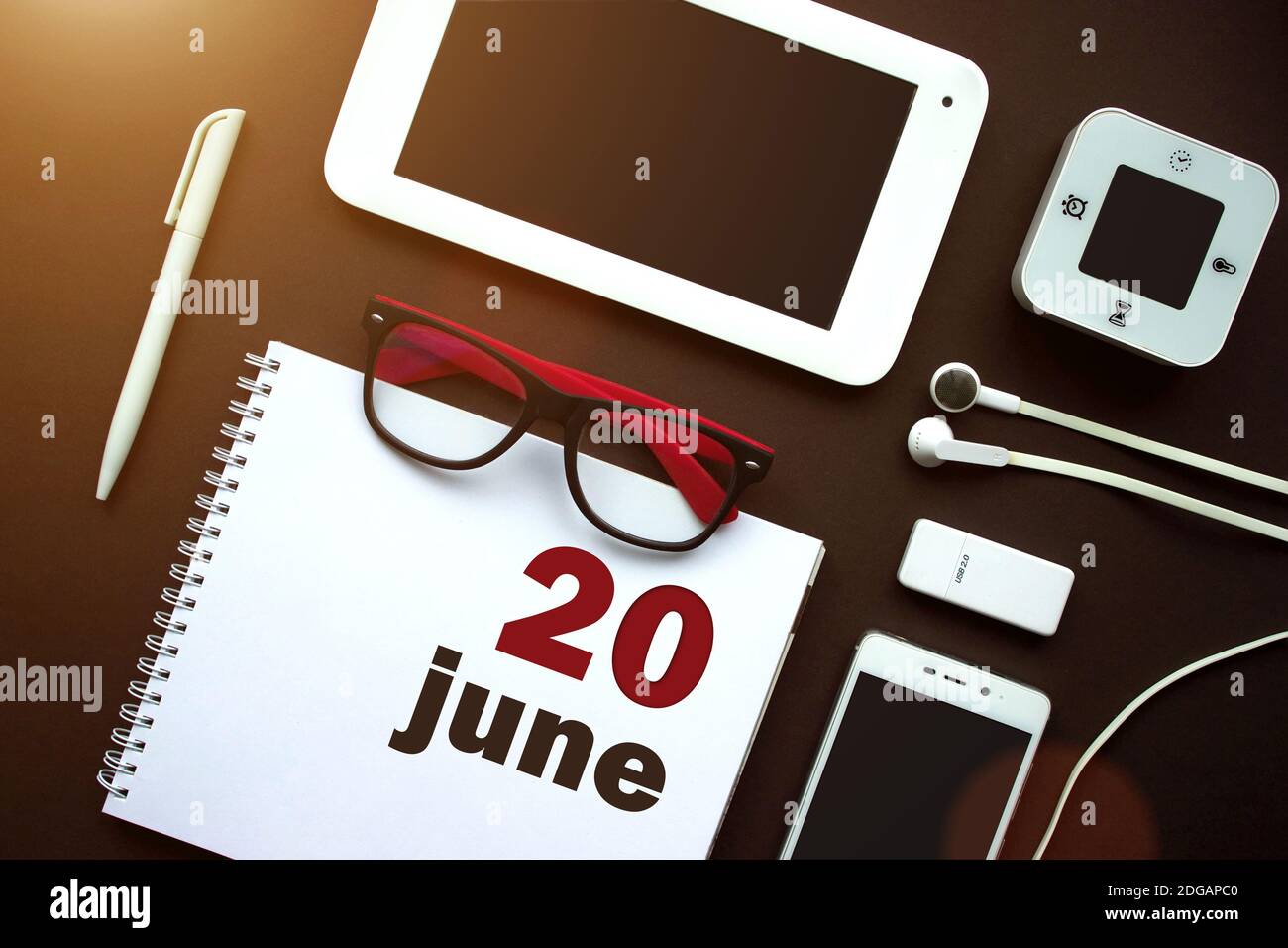 June 20th. Day 20 of month, Calendar date. Office workplace with laptop, notebook, office supplies and stationery on brown back. Summer month, day of Stock Photo