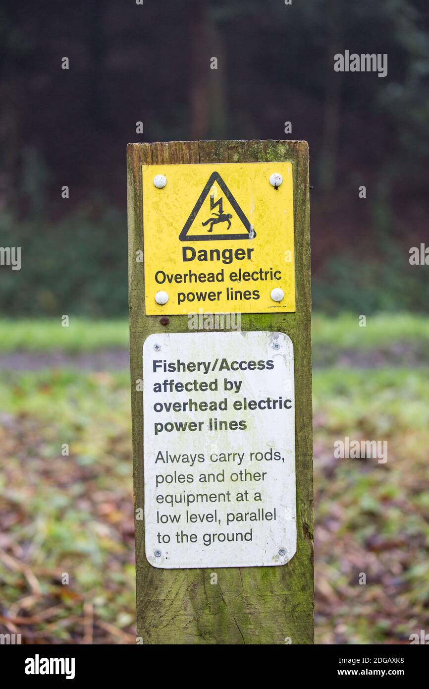 UK danger sign on isolated signpost outdoors on canal towpath, warning fishing, angling public of overhead electric power lines. Stock Photo
