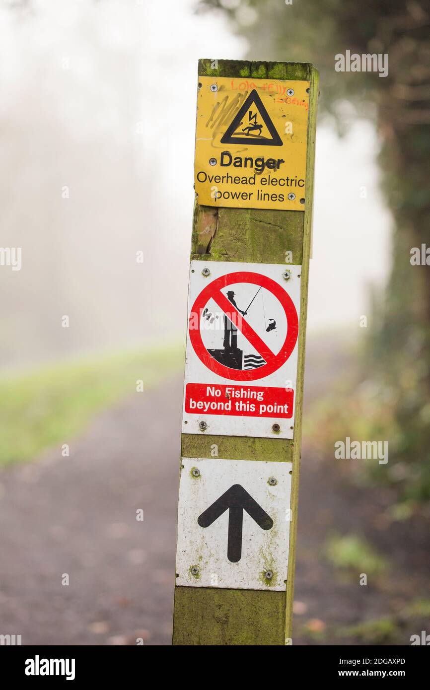 information sign post, danger overhead electric power lines, no fishing on a canal path Stock Photo