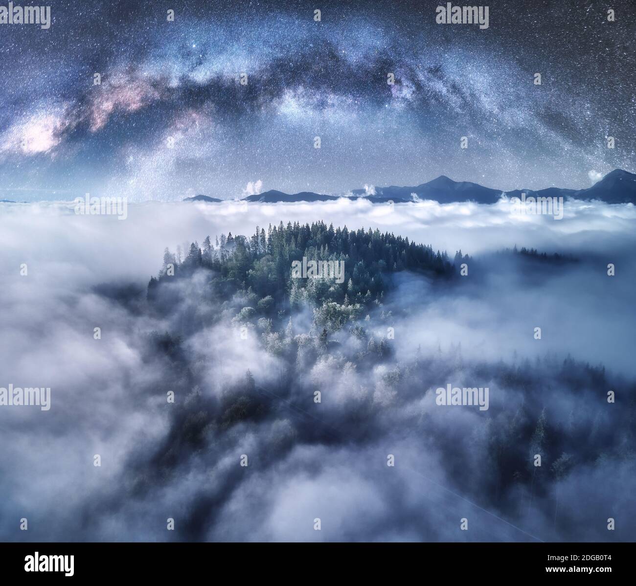 Milky Way arch over the mountains in low clouds at starry night Stock Photo