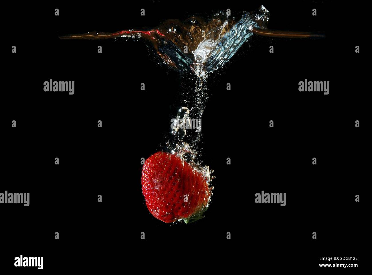 Fresh healthy strawberry falls quickly in water and injected and produced bubbles with black background Stock Photo