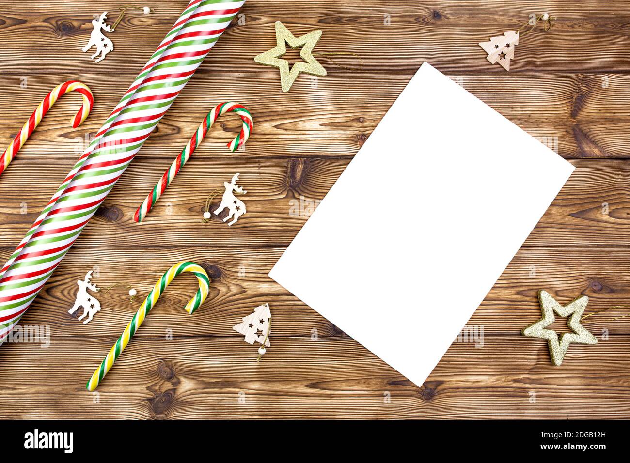 Christmas decorations, wrapping paper, candy canes, a white blank sheet of paper on a wooden background. Flat lay. Stock Photo