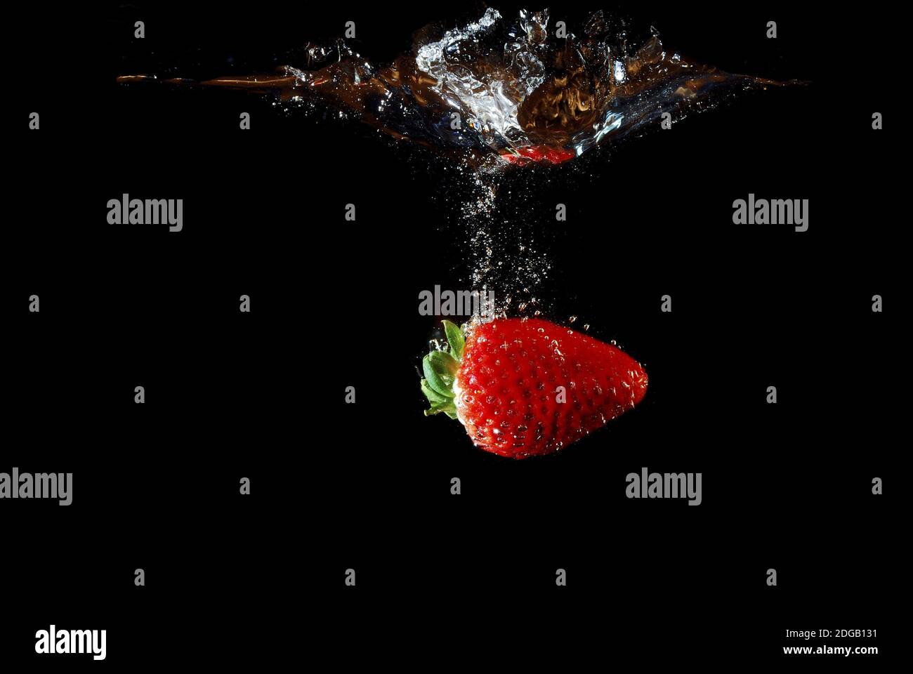 Fresh healthy strawberry falling into water and injected and produced bubbles with black background Stock Photo