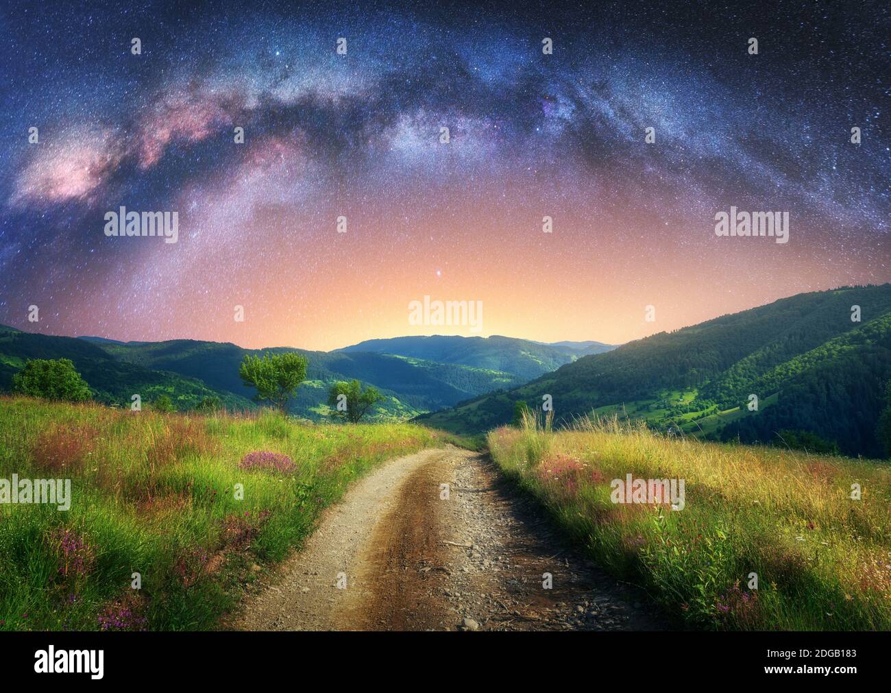 Arched Milky Way over the dirt mountain road in summer at night Stock Photo