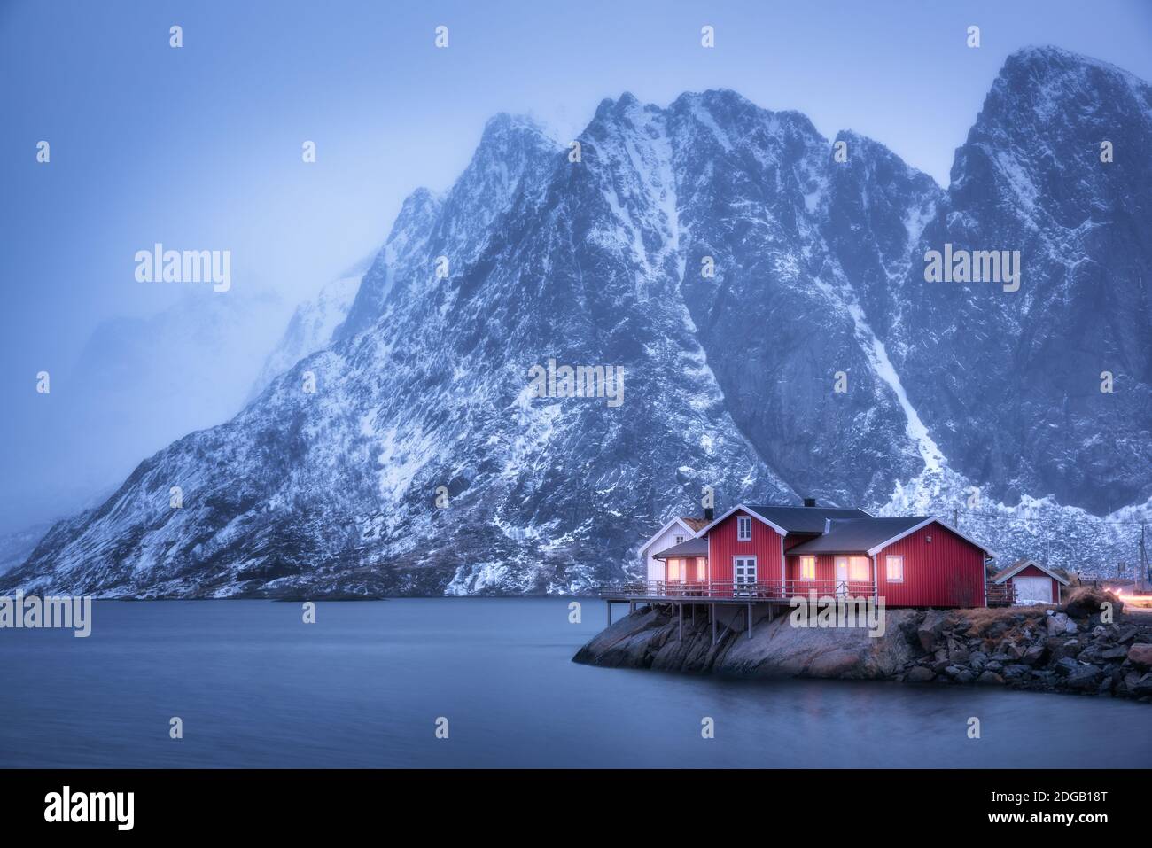 Red rorbu on sea coast and snow covered mountain at dusk Stock Photo