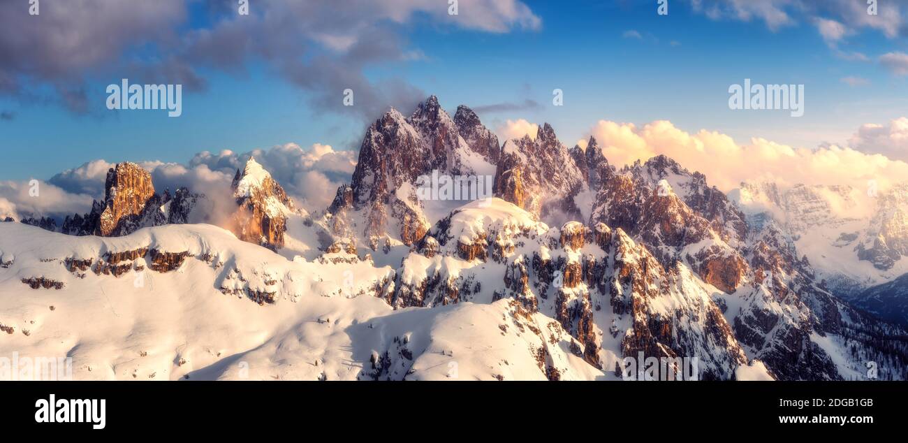Snowy mountains in low clouds and blue sky at sunset in winter Stock Photo