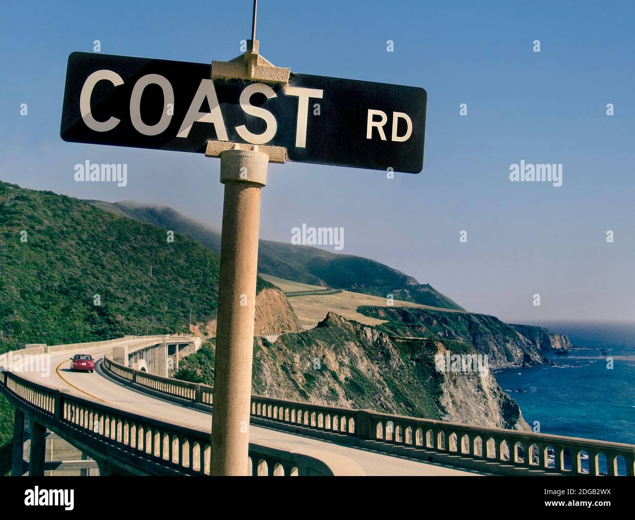 BIXBY BIG SUR CALIFORNIA RETRO Highway 1 Bixby Bridge ‘Coast Road’ sign retro 1960’s style America travel concept with red car crossing Bixby Bridge at Big Sur, Monterey, California USA Stock Photo