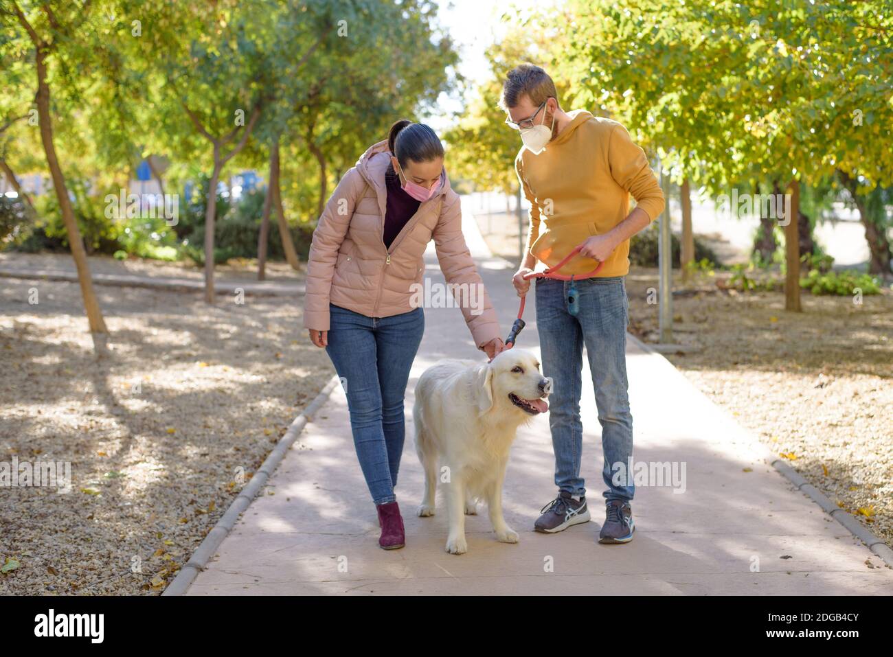 Young white couple in medical surgical masks holding walks with dog in the summer forest. family, europe, hugs, coronavirus, illness, infection Stock Photo