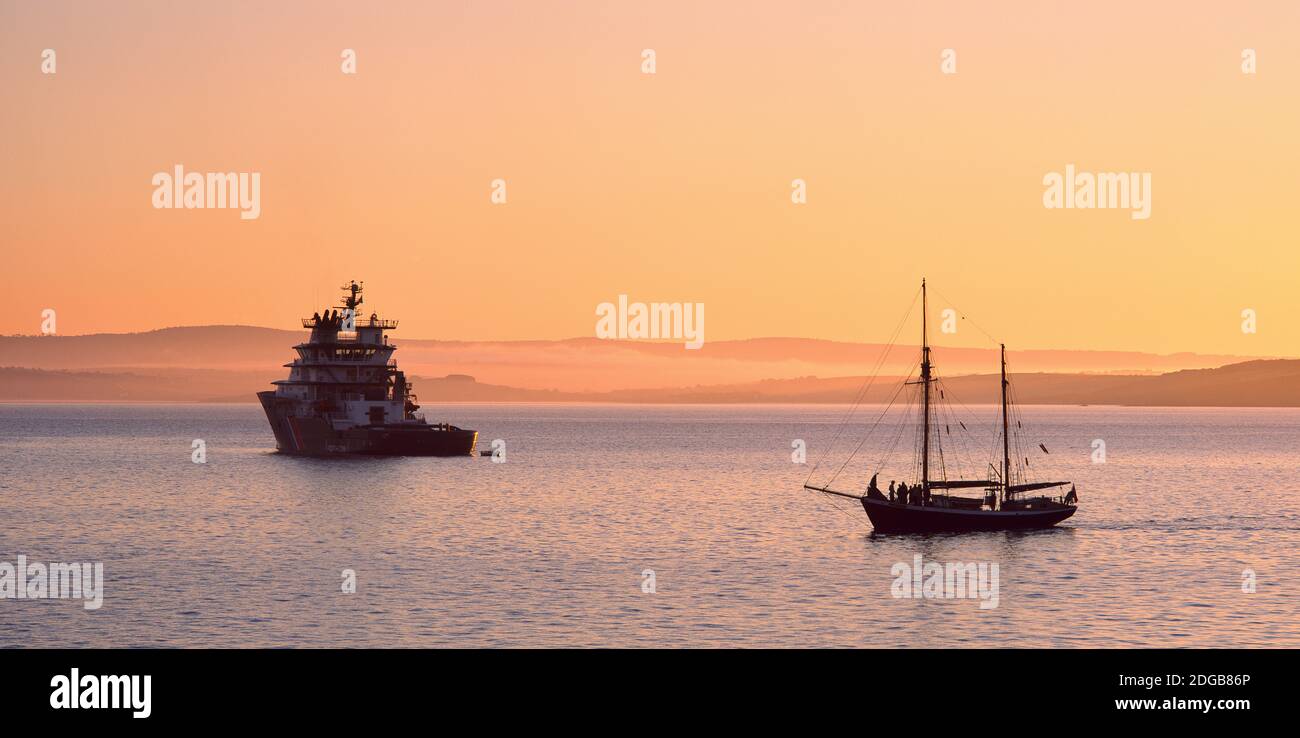 Tugboat and a tall ship in the Baie de Douarnenez at sunrise, Finistere, Brittany, France Stock Photo