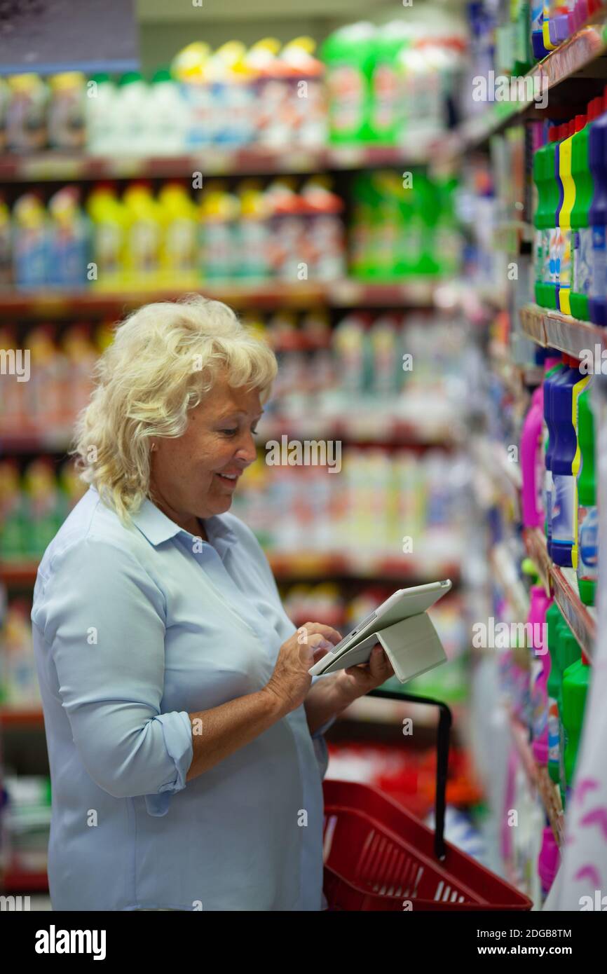 A middle aged woman with a tablet in a household section of a supermarket Stock Photo