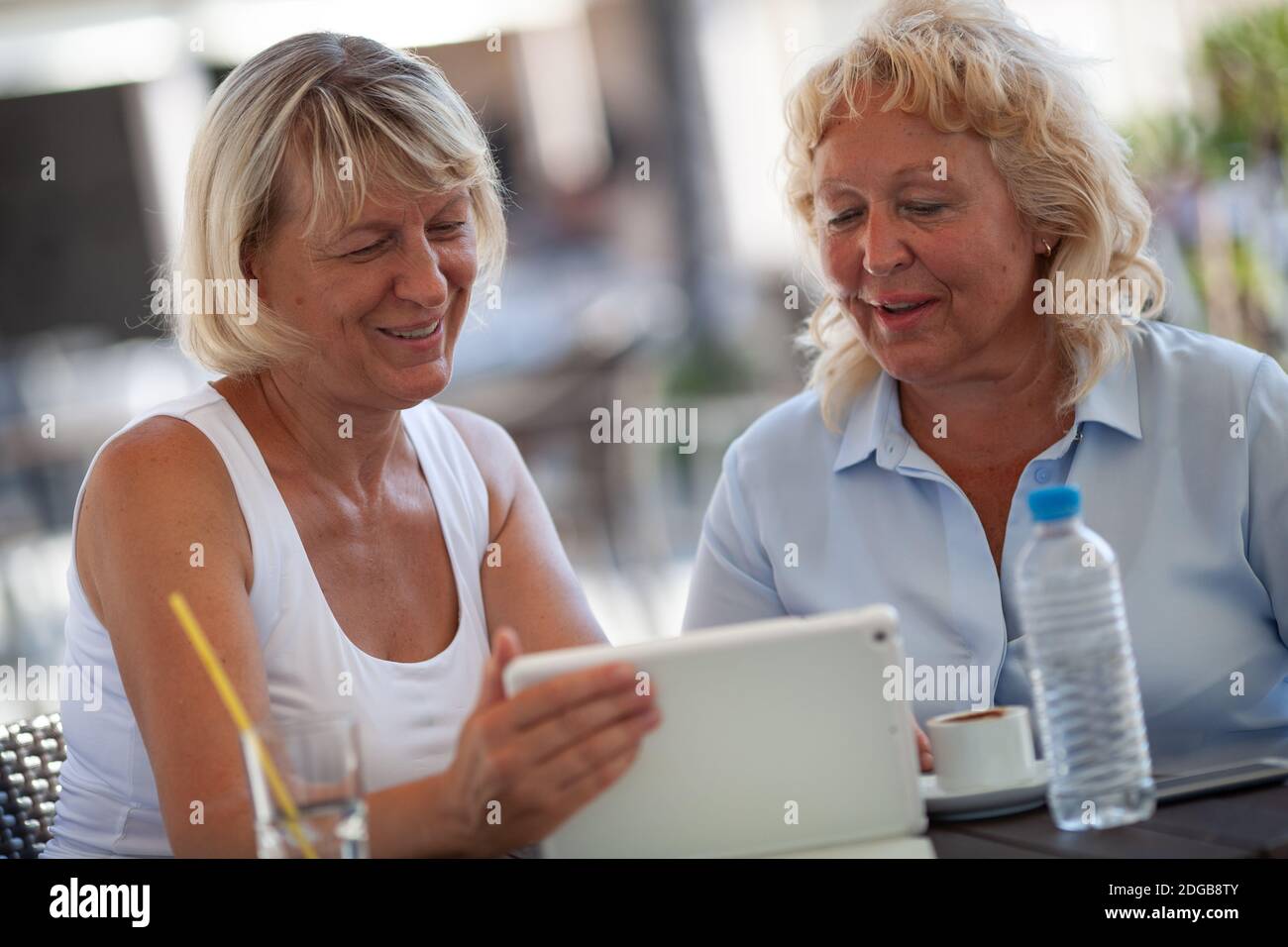 Two smiling senior women at a table of an outdoor cafe looking at the tablet screen Stock Photo
